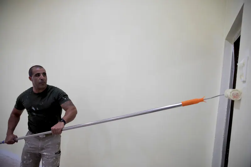 Pintor passando rolo numa parede branca, num ambiente claro